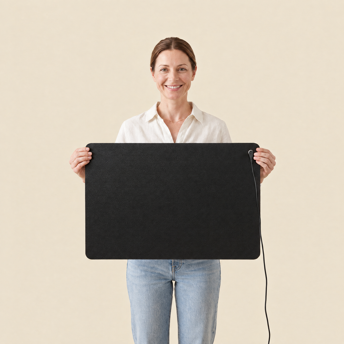 Une femme présente le tapis de mise à la terre Ancorya face caméra, cordon noir clipsé sur le bouton pression.